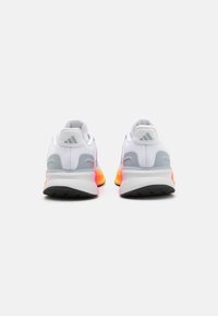 Un paio di scarpe da corsa bianche con accenti grigi e arancioni, viste da dietro su uno sfondo bianco uniforme.