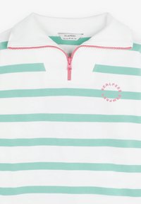 Polo shirt blanc avec des rayures vertes, col haut et fermeture éclair rose. Présente un logo rose sur le côté gauche. Tissu doux et texturé.