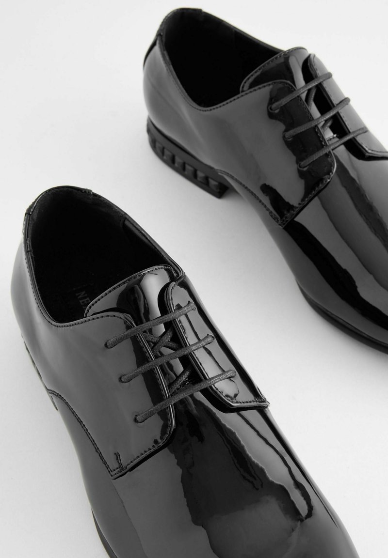 Schwarze Lackleder-Dressschuhe mit einer glatten, glänzenden Oberfläche, runden Zehen und Schnürsenkeln mit einem dezenten Griffmuster auf der Sohle.