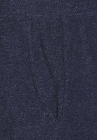 Marineblaues Frotté mit weicher Textur, ausgestattet mit einem V-förmigen Taschendetail. Das Material wirkt saugfähig und ist dick gewebt.