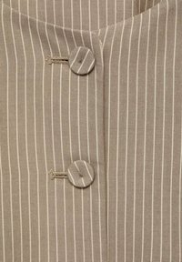 Tessuto a righe beige e crema con collo rotondo, caratterizzato da due bottoni rotondi con motivi testurizzati e un dettaglio di cucitura verticale.