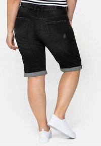Black denim shorts with rolled cuffs, five-pocket design, and a slight distressed detail on the back. Paired with white sneakers.