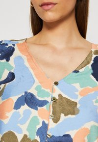 Blusa a maniche corte con scollatura a V, motivo astratto multicolore e cinque bottoni di chiusura frontale. Realizzata in tessuto liscio.