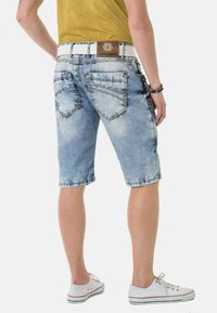 Hellblaue Denim-Shorts mit einem ausgeblichenen Look, die fünf Taschen, kontrastierende Nähte und einen logobehängten braunen Bund aufweisen. Getragen mit weißen Sneakers.