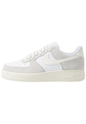 Niskie białe i jasnoszare buty sportowe Nike Air Force 1 z białymi sznurówkami, perforowanym noskiem i fakturowaną podeszwą.