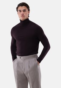 Dunkellila Rollkragenpullover, figurbetontes Design, glatte Textur. Kombiniert mit hellgrauen plissierten Hosen mit Knopf und seitlichen Akzenten.