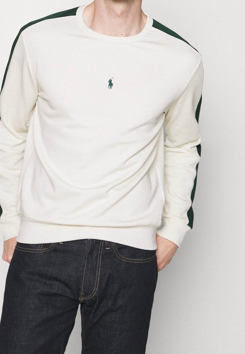 Mikina s kulatým výstřihem v off-white barvě s tmavě zelenými akcenty na ramenou, s malým vyšívaným logem na hrudi. Měkká texturu látky.