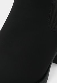 Gros plan d'une chaussure en cuir noir montrant une surface supérieure lisse et un panneau latéral élastique pour un enfilage facile.