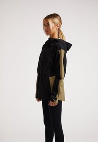 Svart och beige vattentät jacka med huva, utrustad med stora sidofickor och en slank, figursydd design. Slen yta, modern klipp.