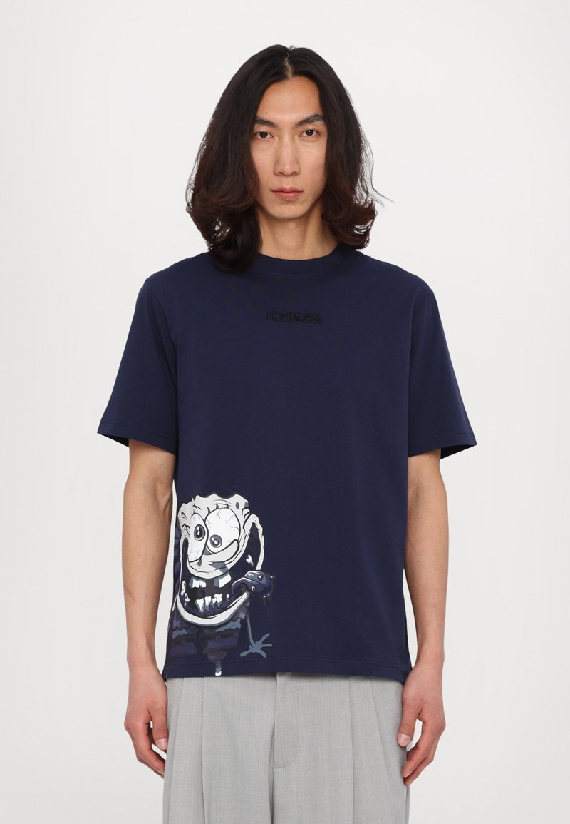 Marineblå bomulds T-shirt med et stort grafisk tryk af en tegneseriefigur på den nedre venstre side og tekstureret logo detaljer på forsiden.
