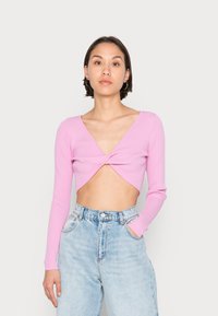 Top cropped de manga longa em rosa com textura canelada, apresenta um detalhe de torção na frente, decote em V e silhueta ajustada, combinado com jeans de cintura alta.