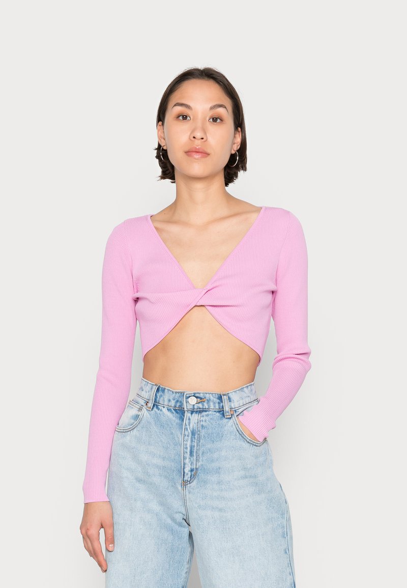 Top cropped de manga longa em rosa com textura canelada, apresenta um detalhe de torção na frente, decote em V e silhueta ajustada, combinado com jeans de cintura alta.