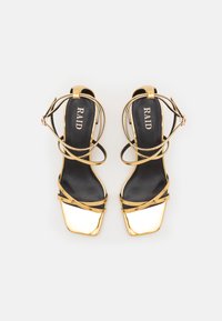 Gold strappy sandals with a square toe design, featuring a shiny metallic toe cap and a black insole labeled "RAID."