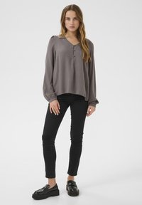 Långärmad grå blus med V-ringning, tre knappar framtill och puffärmar, matchad med svarta slim fit jeans och svarta loafers.