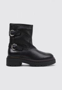 Bottine en cuir noir avec une finition texturée, dotée de deux boucles en argent, d'une semelle épaisse et de détails de couture subtils.