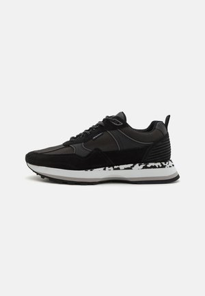 Scarpe sportive nere realizzate con un mix di materiali in rete e suede, dotate di una suola decorata e dettagli testurizzati, con un design arrotondato.