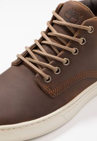 Bruine leren schoen met lichtbruine veters, ronde neus, contrasterende stiksels en rubberen zool. Bevat een boomlogo dat op de tong is gedrukt.