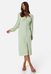 Abito verde chiaro a maniche lunghe con tessuto testurizzato, chiusura a bottoni e design di lunghezza intermedia, caratterizzato da una vestibilità rilassata e leggera svasatura all'orlo.