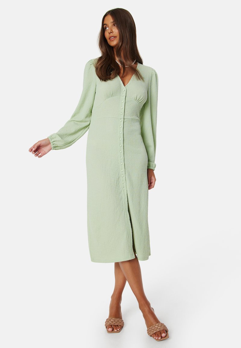 Abito verde chiaro a maniche lunghe con tessuto testurizzato, chiusura a bottoni e design di lunghezza intermedia, caratterizzato da una vestibilità rilassata e leggera svasatura all'orlo.