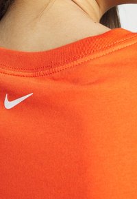 Orange T-shirt med ribbad krage, prydd med en vit Nike-logotyp på vänster sida, tillverkad av mjukt och slätt tyg.