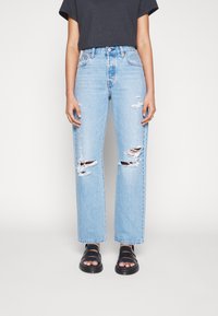 Ljust blå rivna jeans med rak benmodell, tillverkade av denim, med slitningar och hög midja. I kombination med svarta sandaler.