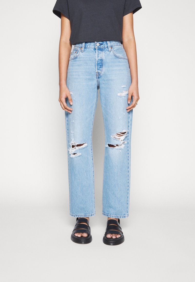 Ljust blå rivna jeans med rak benmodell, tillverkade av denim, med slitningar och hög midja. I kombination med svarta sandaler.