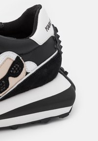 Baskets noir et blanc en daim et cuir, design unique avec une semelle épaisse, des accents texturés et un marquage visible.