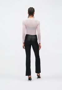 Haut en maille rose pâle à manches longues et jean noir évasé avec une texture lisse. Le haut présente un col simple. Silhouette slim.