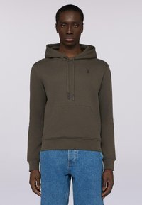 Olivgrön hoodie med textilstruktur, justerbara snoddar, framficka, ribbade manschetter och nederkant. Matchad med ljusblå jeans.