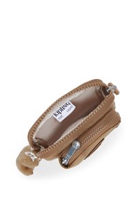 Piccolo astuccio beige Kipling con cerniera principale aperta, etichetta interna visibile, tasca con cerniera frontale e un portachiavi peloso attaccato.