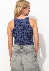 Débardeur sans manches bleu avec un motif léopard noir, associé à un short taille haute gris comportant quatre poches et une texture décolorée.