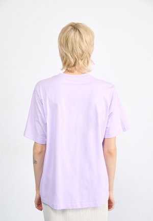 Fialové tričko s krátkým rukávem z měkké látky, s uvolněným střihem a kulatým výstřihem. Pohled zezadu ukazuje jednoduchou, hladkou strukturu bez ozdob.