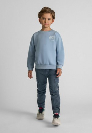 Lyseblå sweatshirts med ribbede manchetter, der har hvid tekst. Sammen med mørkegrå cargobukser med elastiske manchetter og multikolore sneakers.