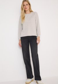 Sweatshirt gris à manches longues avec un col rond, associé à un pantalon large noir et des baskets légères avec des accents bleus.