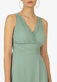 Mintgrünes Kleid aus leichtem Stoff, mit plissierten Details im Oberteil und einem glatten Taillenbund, sowie einem V-Ausschnitt.
