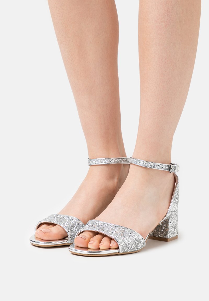 Sandali con glitter argento, dotati di una cinturino alla caviglia, design aperto sulla punta e tacco a blocco. Il materiale riflette la luce, esaltando l'effetto glitter.