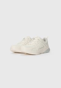 Une paire de baskets de sport blanc cassé avec des superpositions en mesh et en synthétique, un design à lacets et des semelles rembourrées sur un fond blanc uni.