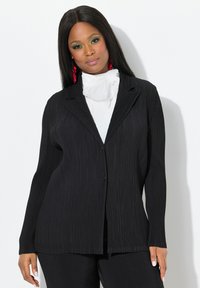 Zwarte, geribbelde blazer met een reverskraag, enkele knoopsluiting, lange mouwen en een ontspannen pasvorm. Draag het over een witte hooggesloten top.