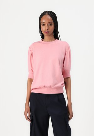 Lys rosa genser med korte puffærmer og rund hals, med en ribbestrikket kant. Kombinert med marineblå bukser.