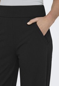 Black trousers with a smooth texture feature a side pocket and a wide waistband, highlighting a minimalist design.