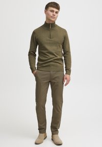 Suéter verde oliva con cuello de media cremallera, puños y dobladillo acanalados. Combinado con pantalones ajustados de oliva a juego y botas de tobillo color beige.