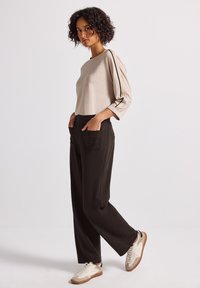 Haut beige à manches longues avec accents noirs et coupe décontractée, associé à un pantalon noir taille haute avec deux poches avant et des baskets.