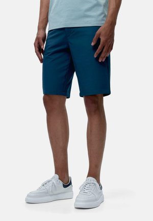 Shorts teal avec une texture lisse, longueur genoux, et poches. Assortis à des baskets blanches avec des accents bleu marine.