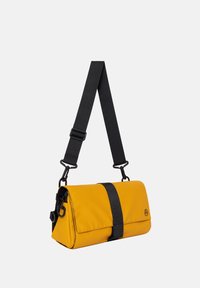 Borsa in tessuto gialla con tracolla nera, forma rettangolare, patta pieghevole e dettagli neri. Presenta hardware regolabile e dettaglio del logo.