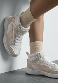 Baskets montantes en blanc, gris et rose ; présentent un design en maille, un rembourrage à la cheville et un laçage à l'avant avec sangle en velcro. Matériaux texturés visibles.