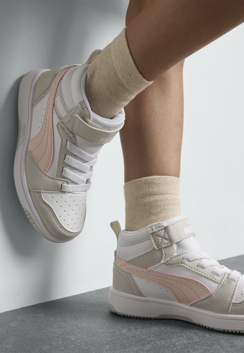 Baskets montantes en blanc, gris et rose ; présentent un design en maille, un rembourrage à la cheville et un laçage à l'avant avec sangle en velcro. Matériaux texturés visibles.