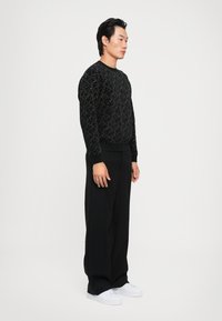 Pulover negru tricotat cu un model texturat, cu manșete și tiv texturat, combinat cu pantaloni negri pliați și adidași albi.