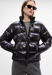 Melns pūkains jaka ar spīguļojošu apdari, ar augstu apkakli, rāvējslēdzēju un sānu kabatām. Valkāta virs svītrainas krekla.