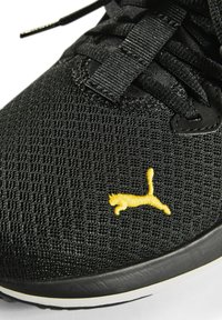Zwarte ademende mesh sneaker met een gele geborduurde logo, textuur bovenkant en zwarte veters met een wit en zwart loopvlak.