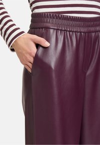 Bordeauxkleurige neplederen broek met een elastische tailleband, zijzakken en een gladde textuur, gecombineerd met een gestreepte lange mouw top.